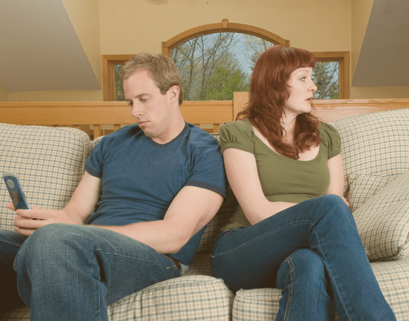 man and woman sitting on couch not paying attention to each other