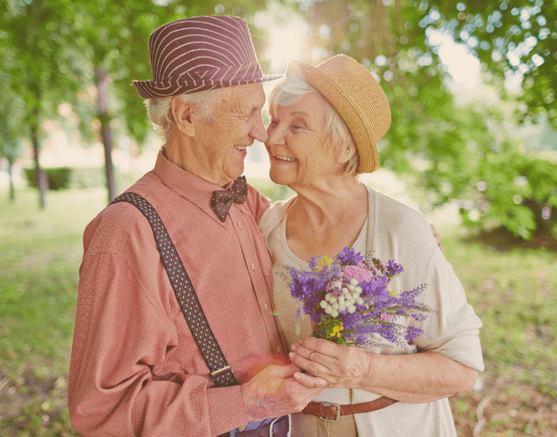 older man and woman standing outside hugging each other and flowers sun shining smiling at each other