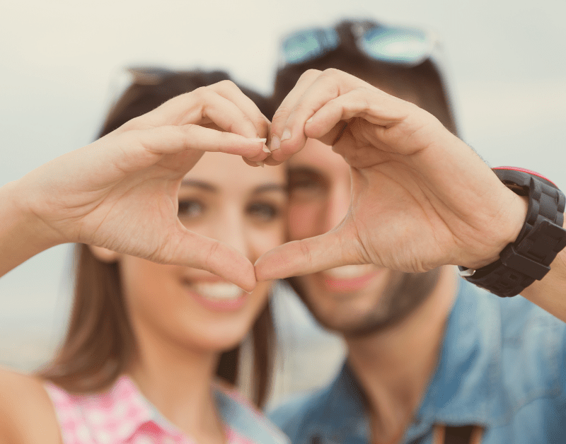 man and woman outide smiling and holding their hands together in the shape of a heart