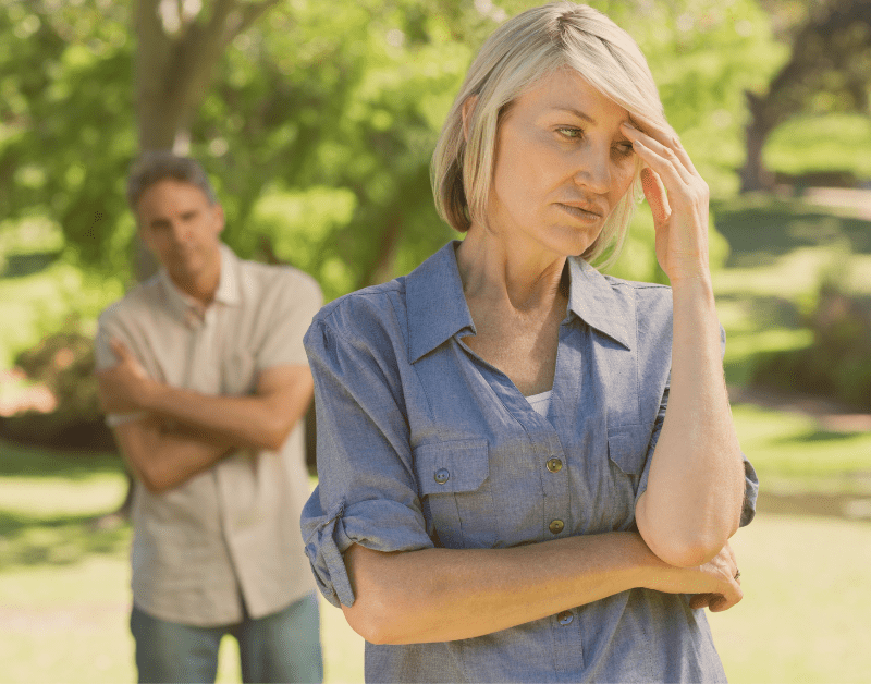 woman standing outside looking frustrated and sad while man stands in the background