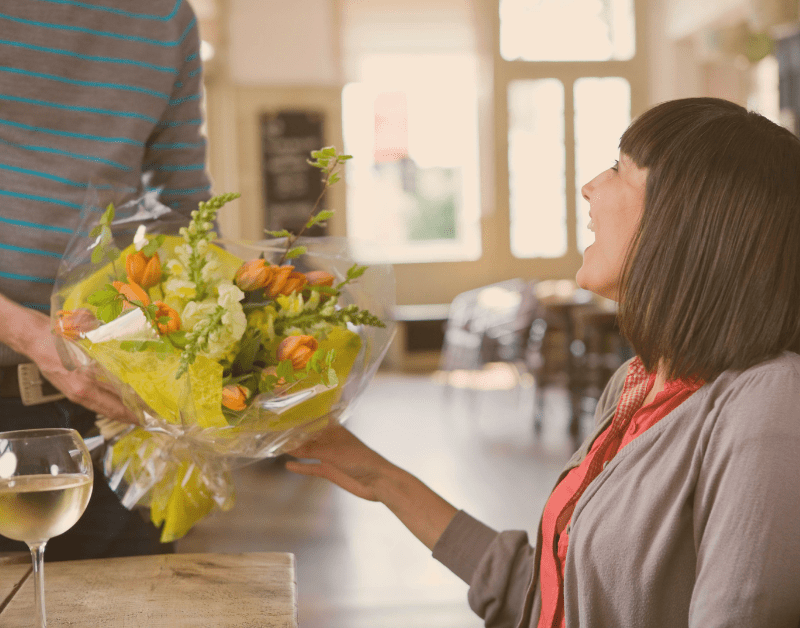 man giving flowers to woman while woman smiles at him