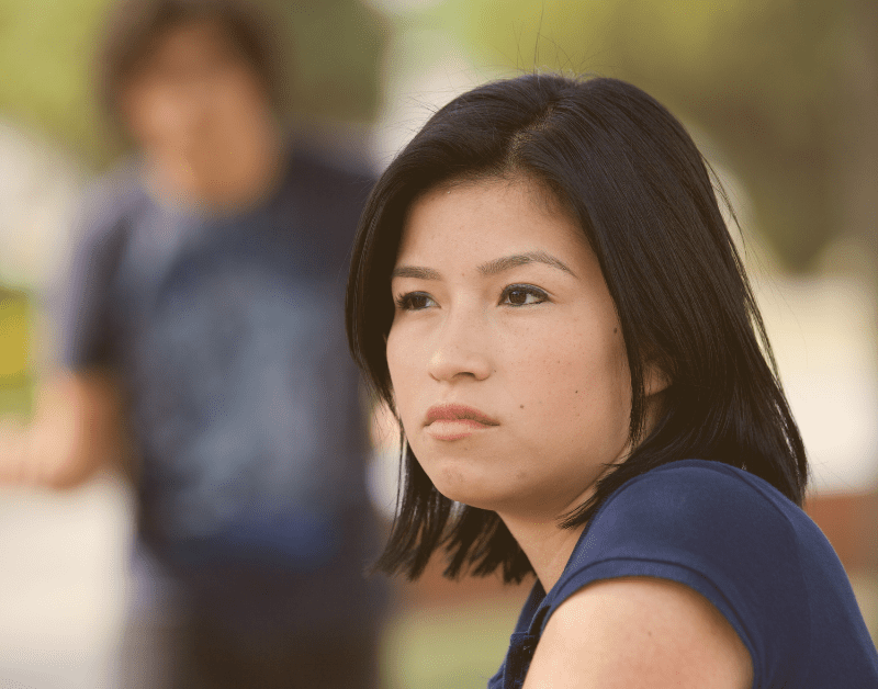woman sitting looking off into distance man behind her blurred out