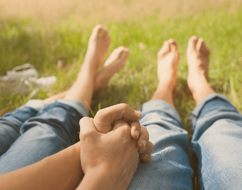 holding hands while sitting on the grass outside in the sun
