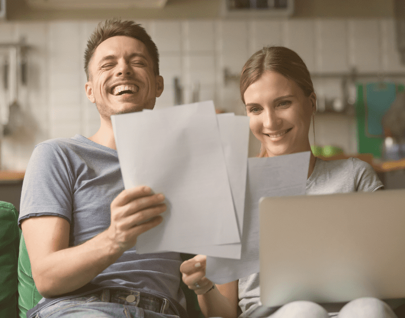 man and woman looking at papers while sitting on the couch laughing and smiling