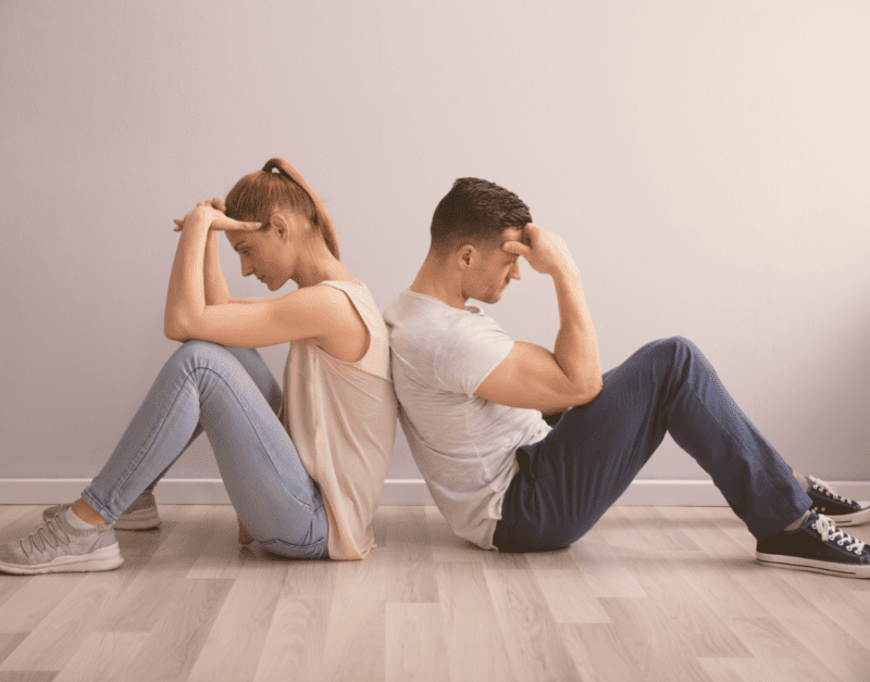 man and woman at odds sitting back to back on the floor