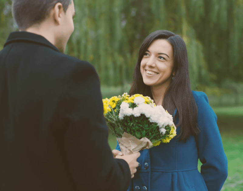 man handing flowers to smiling woman outside