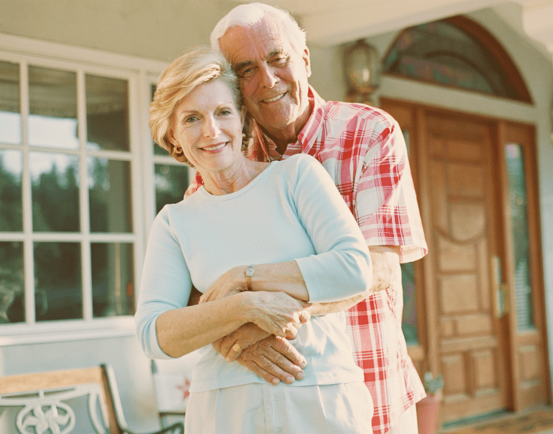 older couple standing in front of house hugging and happy