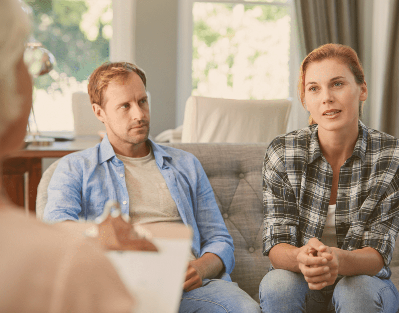 man and woman sitting on couch talking to third party