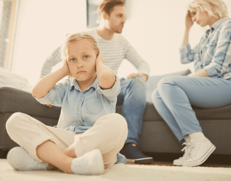 couple sitting on couch arguing while child sits on floor covering her ears